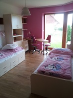 Finální realizace interiéru dětského pokoje, záběr na postele, židle, stůl, okno do zahrady a skříň