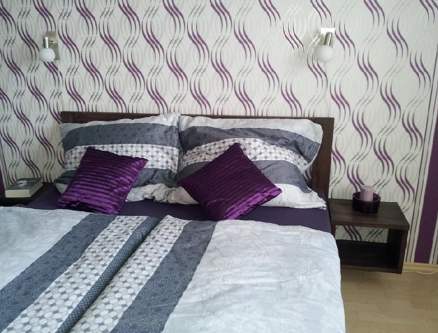 Finální realizace interiéru ložnice s fialovou dřevěnou postelí a nástěnnou tapetou zblízka