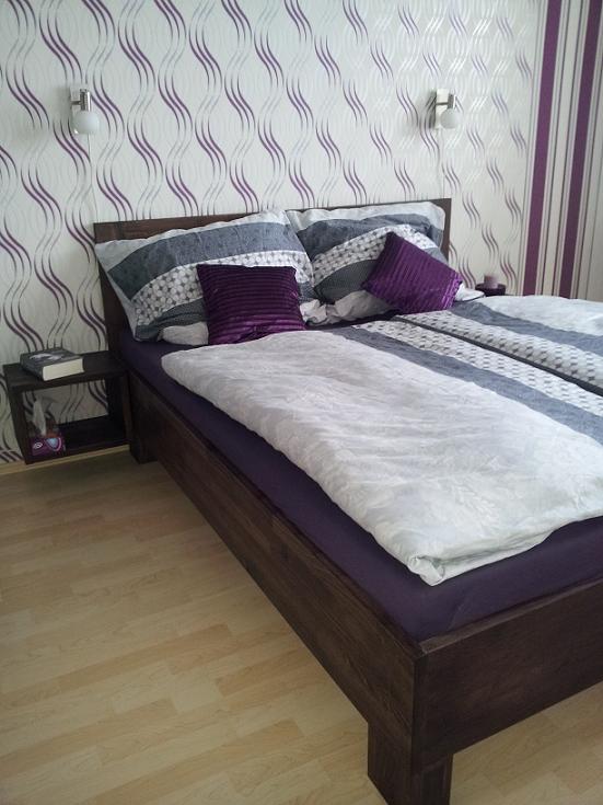 Finální realizace interiéru ložnice s fialovou dřevěnou postelí a nástěnnou tapetou vzdáleně